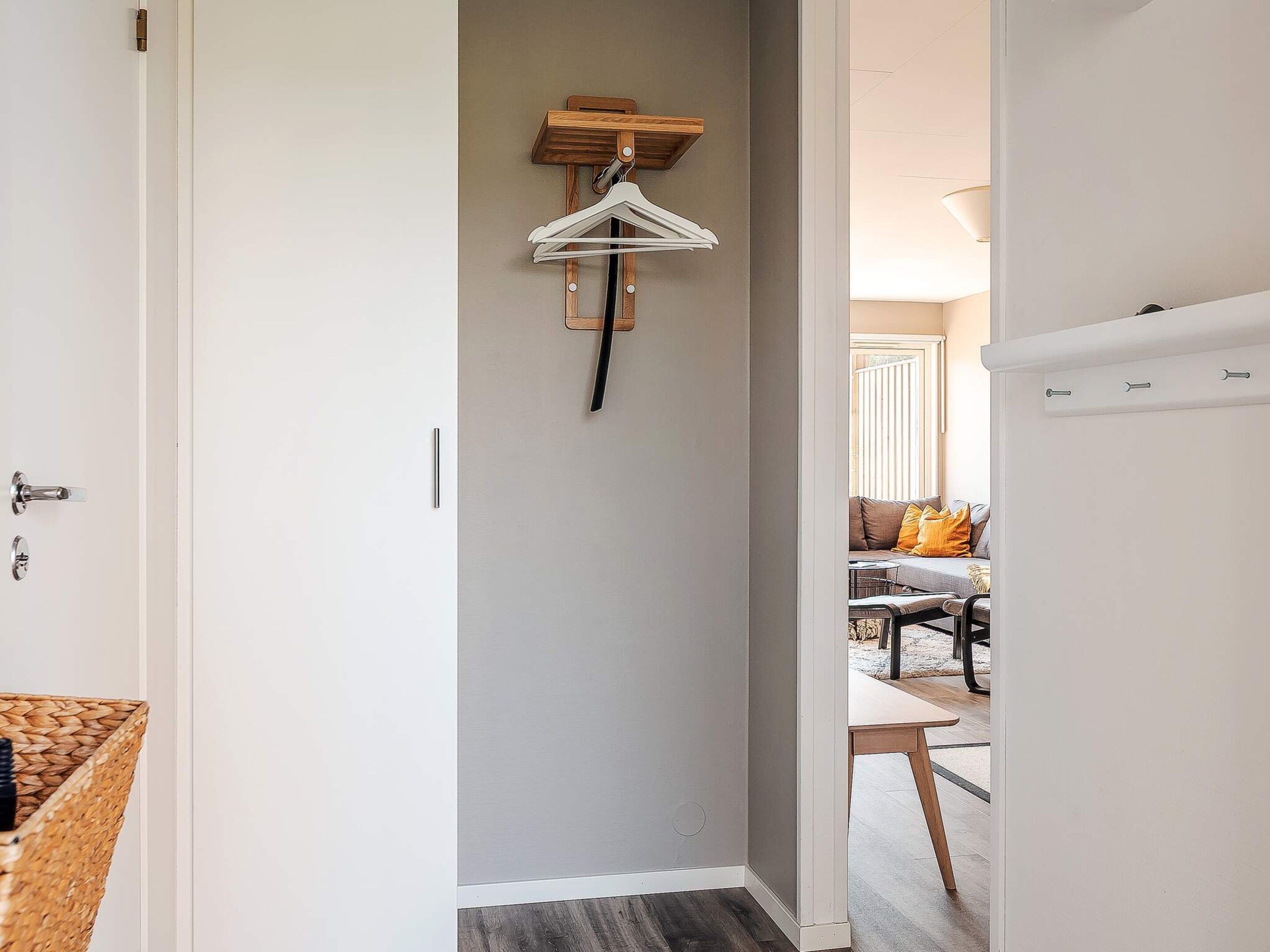 Um corredor com um porta-roupas, uma porta com puxador e um vislumbre de uma sala de jantar com mesa e cadeiras.