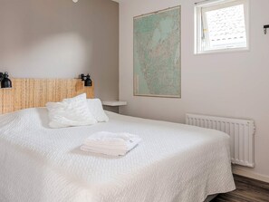Un lit bien fait, recouvert d’une couette blanche, une carte accrochée au mur et une fenêtre avec des stores.