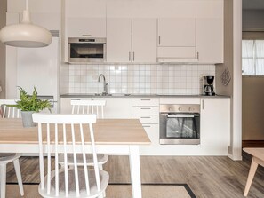 Eine moderne Küche mit weißen Schränken, einem Einbauofen, einer Kaffeemaschine und einem Essbereich mit Tisch und Stühlen.