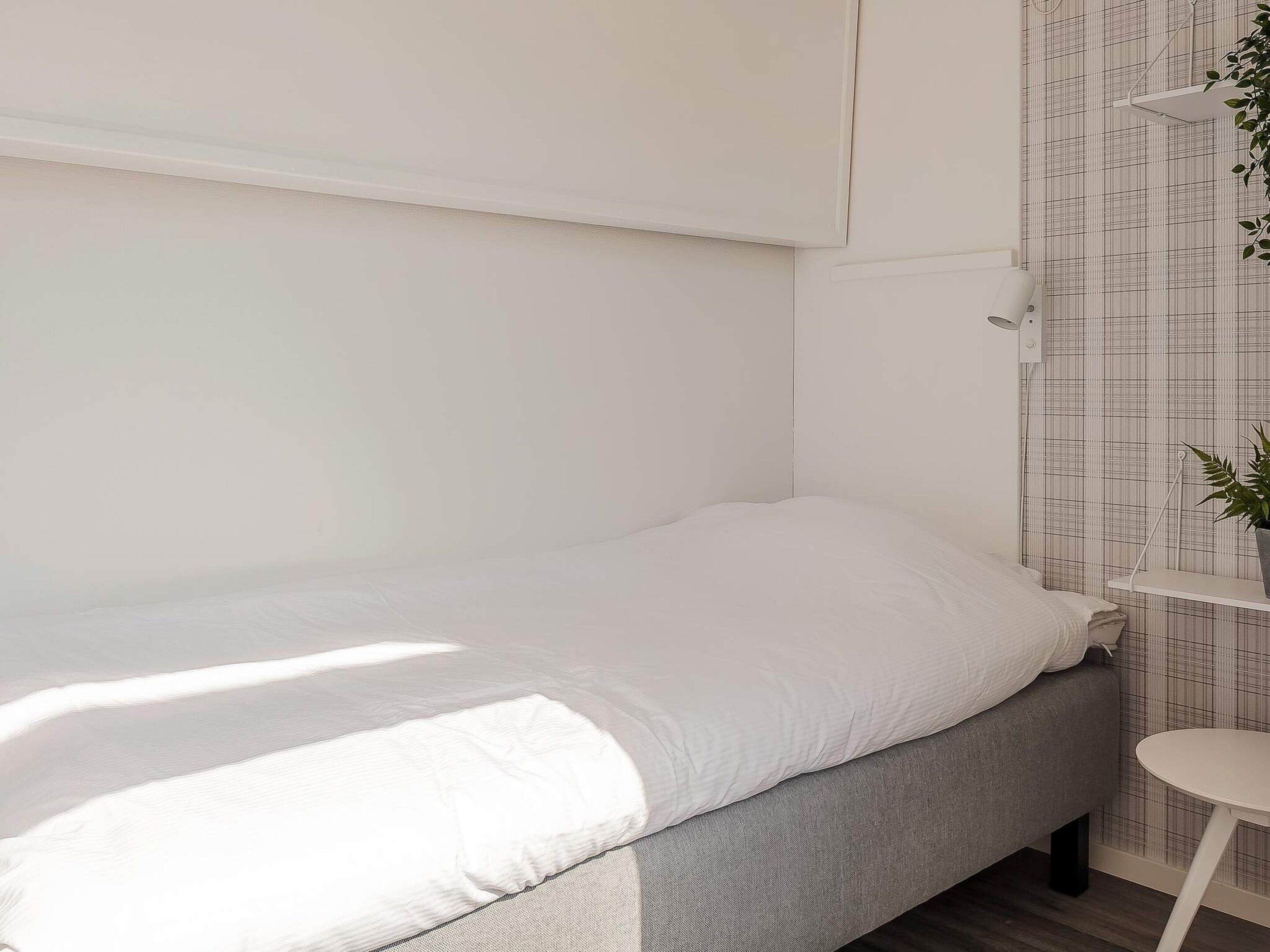 A single bed with a grey headboard, a small bedside table, and a wall-mounted shelf with a plant.