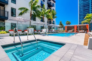 Un área de piscina en la azotea con sillones, sombrillas y palmeras.