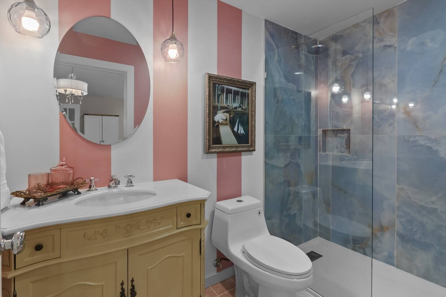 Un bagno con un mobile lavabo, un water, una doccia con pareti in vetro, uno specchio rotondo e un quadro appeso alla parete.