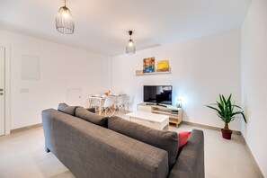 A modern living room with a grey sofa, a TV, a small table, and a potted plant. - LXR Navegante 2-Bedroom Next to the Sea (Fuengirola)