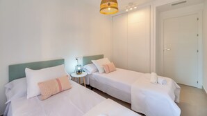 Hotellihuone, jossa on kaksi erillistä sänkyä, yöpöytä lampulla, vaatekaappi ja riippuvalaisin.