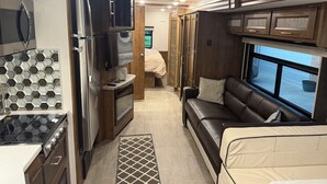 Ein kompaktes Wohnmobil-Interieur mit einer Küchenzeile, einer Sitzecke und einem Fenster mit Blick hinaus.