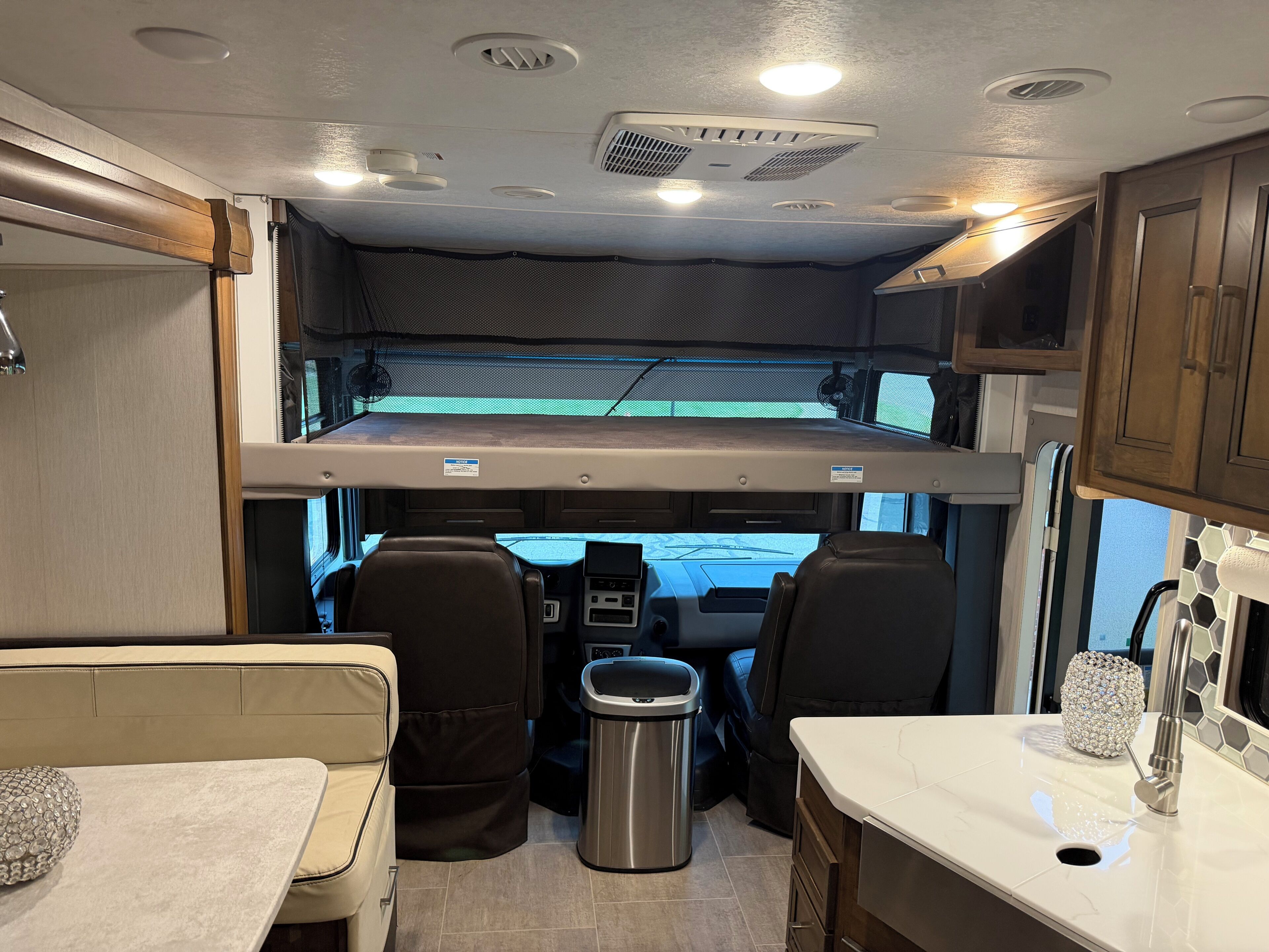Interior compacto de una caravana con kitchenette, zona de comedor y una cama elevada.
