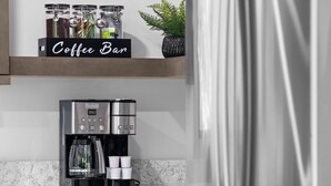 A coffee bar with a coffee machine, cups, and jars on a marble countertop.