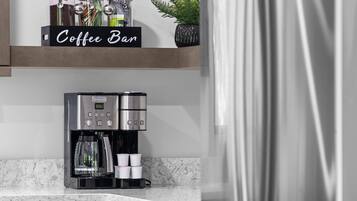 A coffee bar with a coffee machine, cups, and jars on a marble countertop.