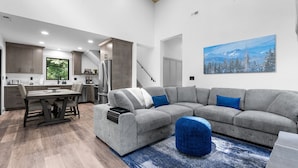 A modern living room with a gray sectional sofa, a dining table, and a kitchen in the background.