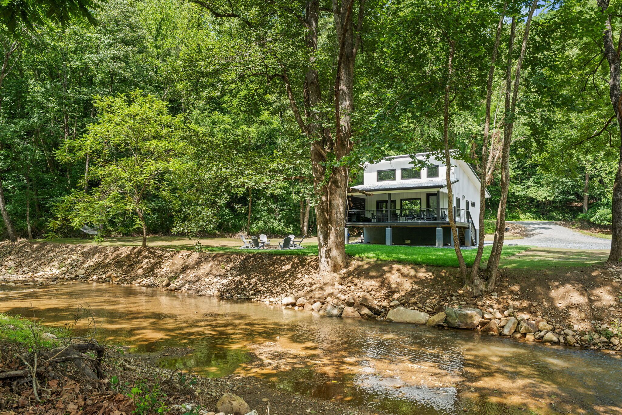 Une maison dotée d’une terrasse, entourée d’arbres et bordée par une rivière.