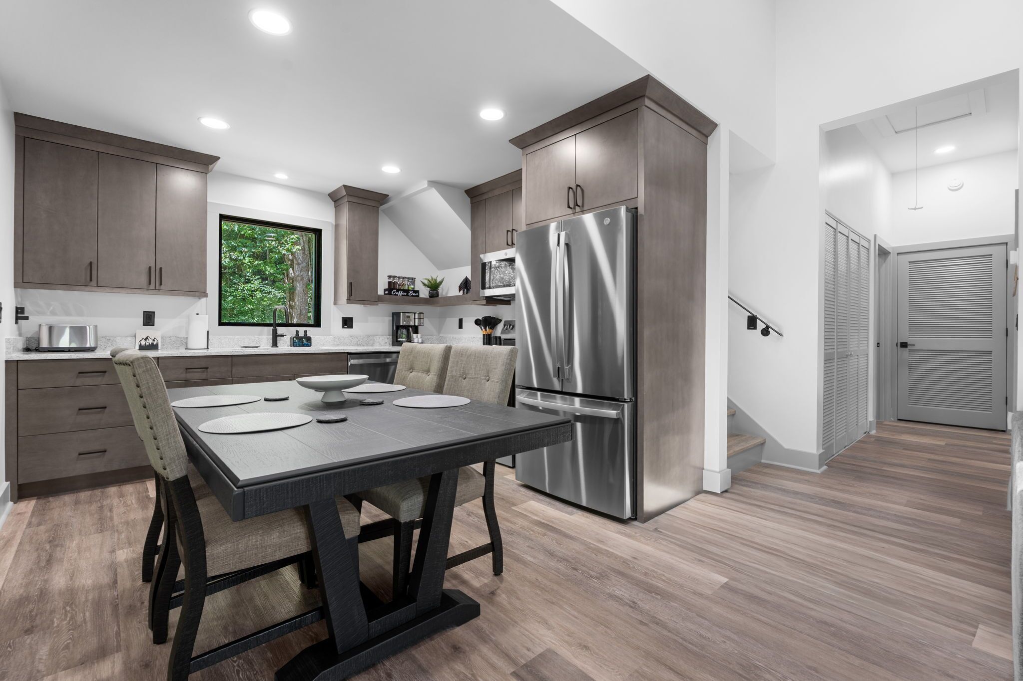 Une cuisine moderne dotée d’un grand réfrigérateur en acier inoxydable, de meubles de rangement en bois foncé et d’une table à manger avec des chaises.
