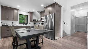 A modern kitchen with a large stainless steel refrigerator, dark wooden cabinets, and a dining table with chairs.