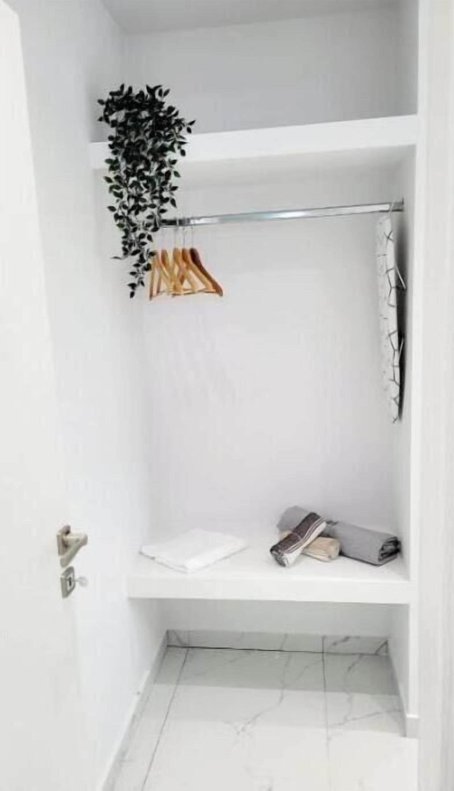 A white bathroom with a shower, a towel rack, and a shelf with folded towels.