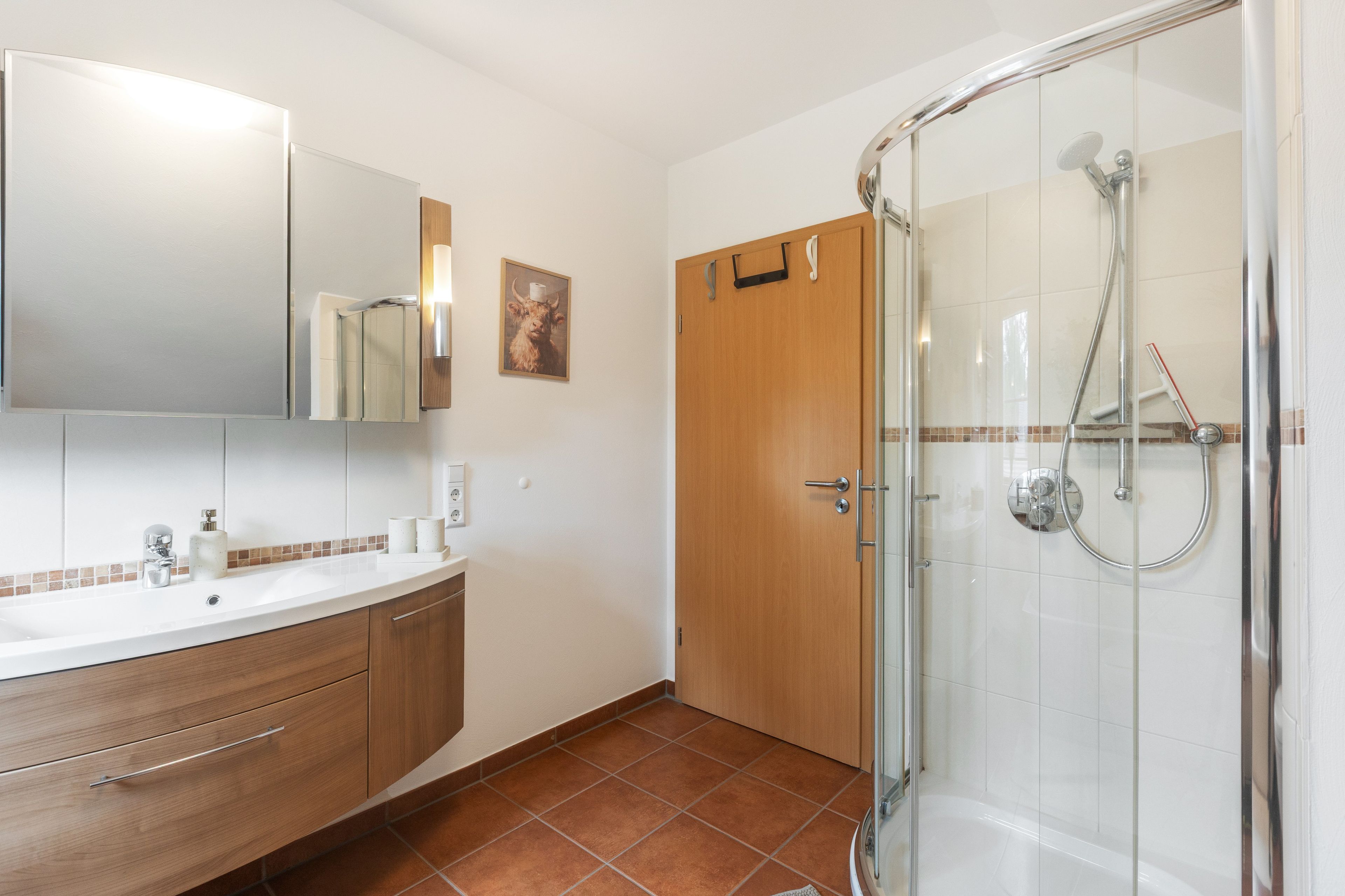 Un baño con cabina de ducha de vidrio, lavabo con espejo y puerta de madera.