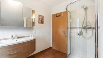 Un baño con cabina de ducha de vidrio, lavabo con espejo y puerta de madera.