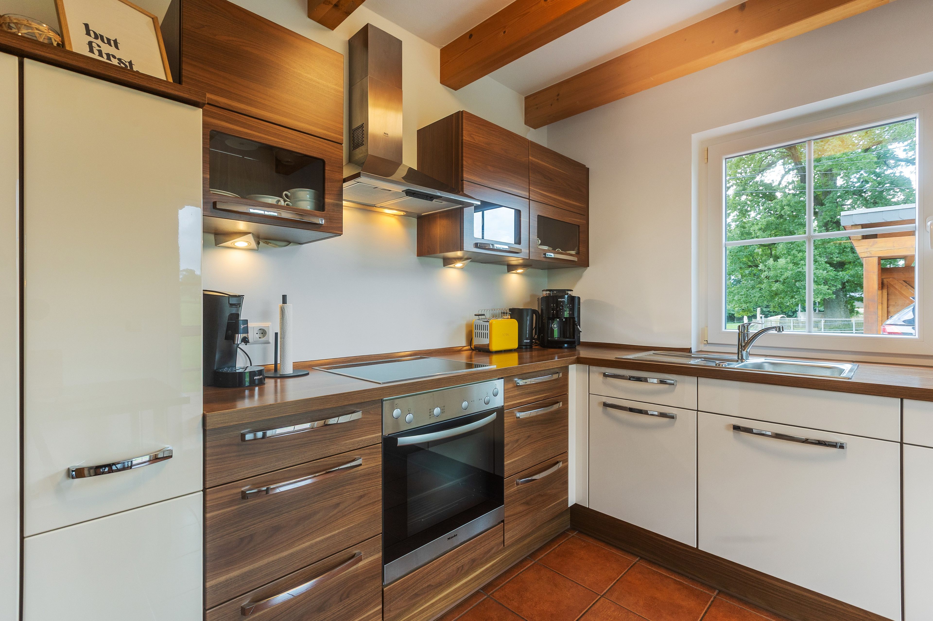 Una cucina moderna con mobili in legno, forno integrato e una finestra con vista su spazi verdi.