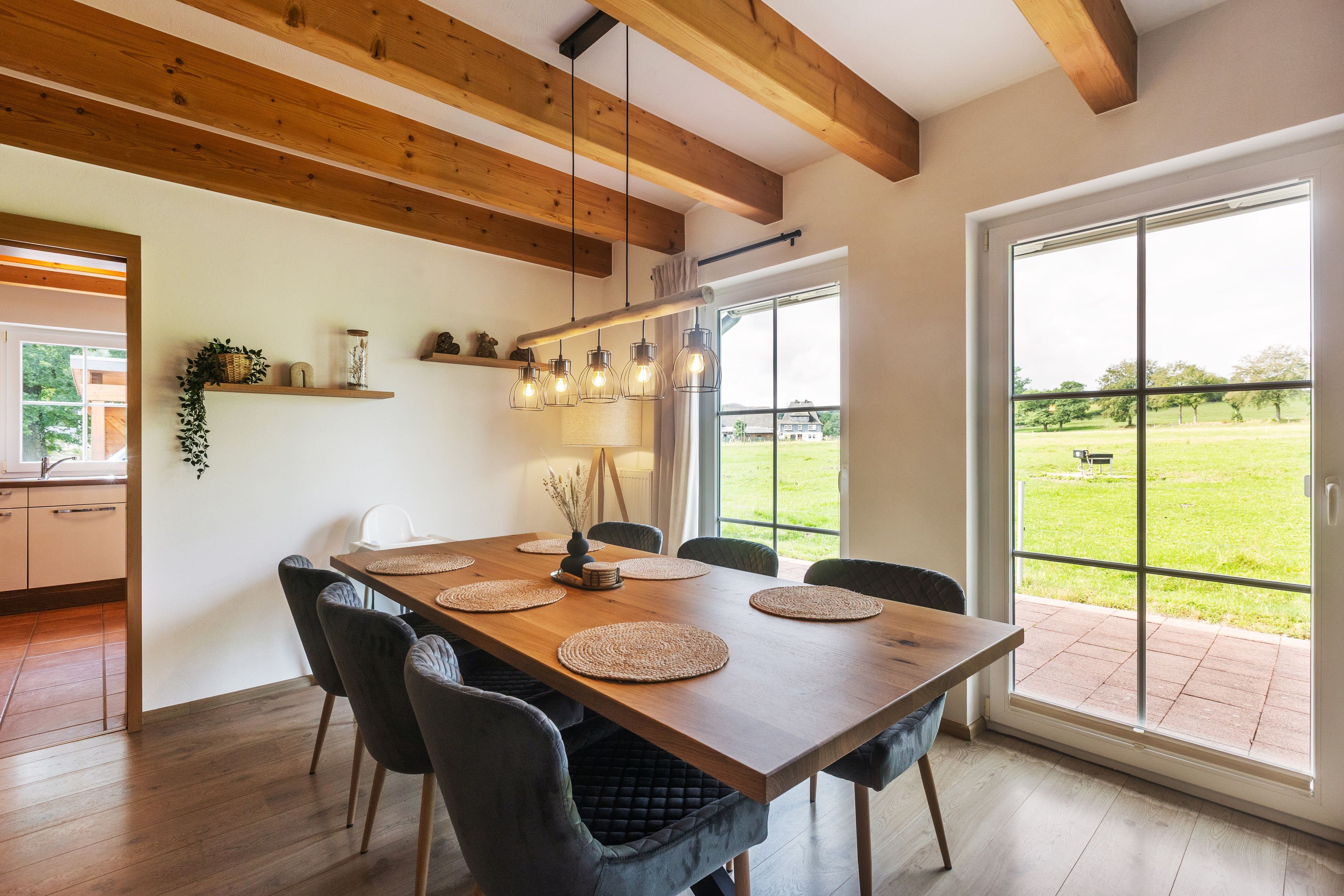 Ein Essbereich mit Holztisch, Stühlen und Blick auf ein grünes Feld durch große Fenster.