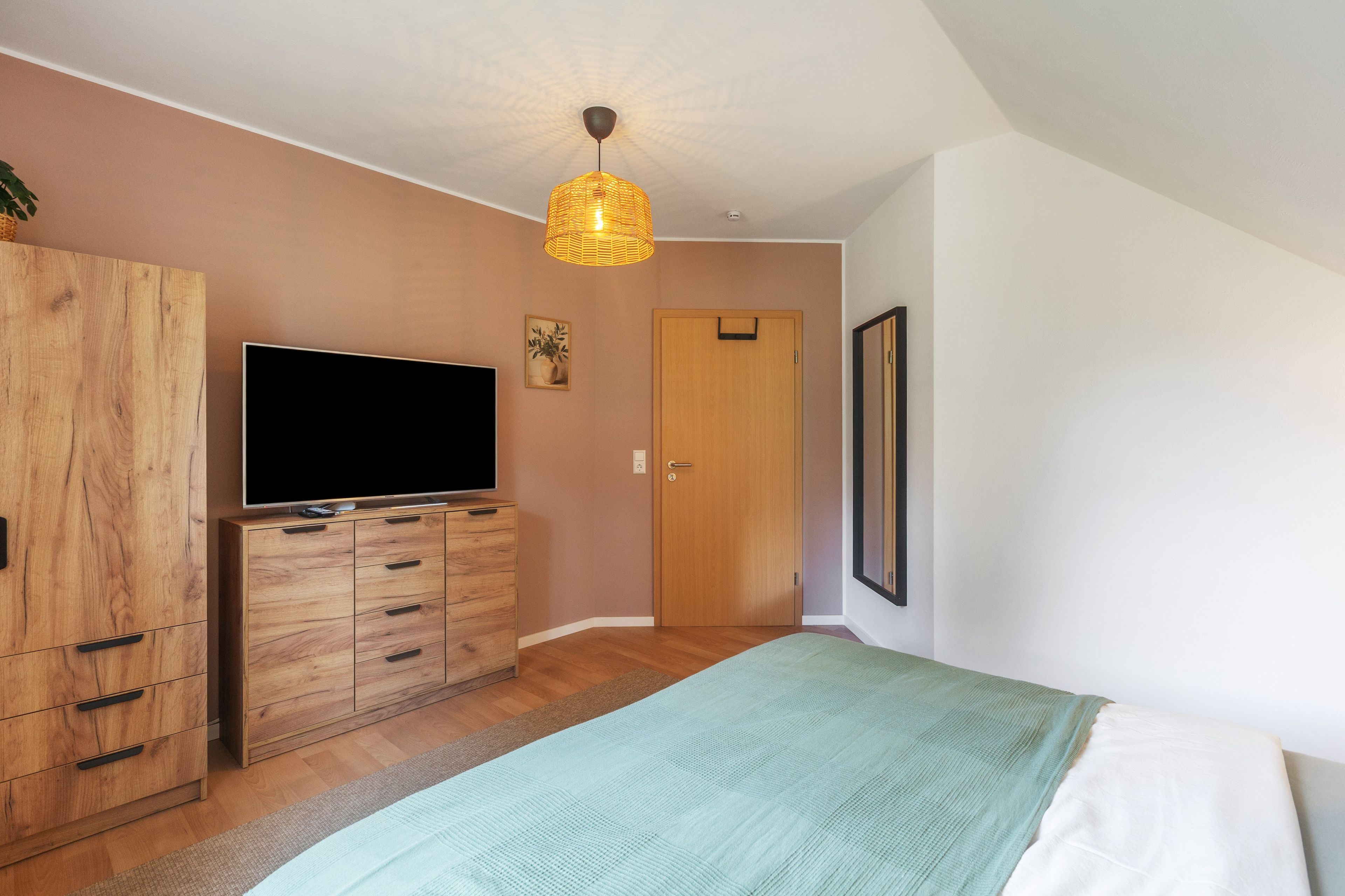 Ein Schlafzimmer mit einem Bett, einem Holzschrank, einem Fernseher und einer Tür.