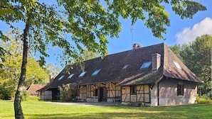 A traditional half-timbered building with a sloped roof, multiple windows, and a surrounding grassy area.