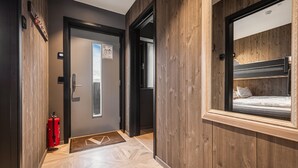 A hallway with a wooden wall, a fire extinguisher, a door, and a window with a bunk bed. - Ski-in / Ski-out apartment in Hemsedal (Hemsedal)