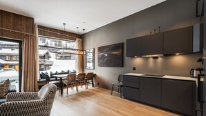 A modern kitchen with dark cabinets, a dining area with wooden flooring, and a view of a snowy village through large windows. - Ski-in / Ski-out apartment in Hemsedal (Hemsedal)