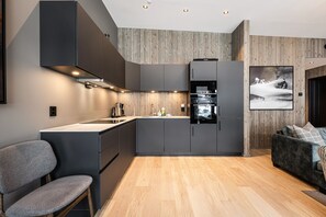 A modern kitchen with built-in appliances, a dining area with a chair, and a sofa. - Ski-in / Ski-out apartment in Hemsedal (Hemsedal)