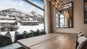 A wooden dining table with benches, a large window with a view of snow-covered buildings and mountains, and a modern light fixture. - Ski-in / Ski-out apartment in Hemsedal (Hemsedal)