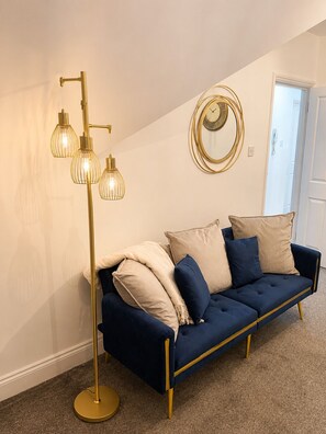 A room with a blue sofa, gold floor lamp, and a round mirror on the wall. - Cozy 2 bedFlat with 50inch TVs (London)