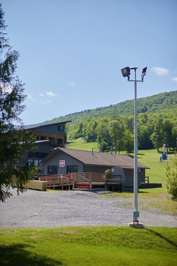A building with a red cross sign, a wooden deck, and a gravel parking area. - Slopeside luxury condo - sleeps 6 – Walk to Timberline Mountain ski lifts and lodge! (Tucker County)