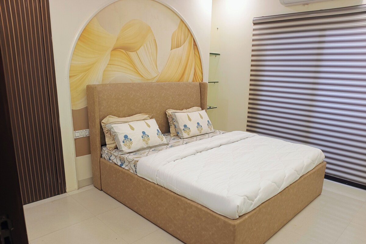 A bed with a beige headboard and white bedding, a wall with a decorative arch, and a window with blinds.