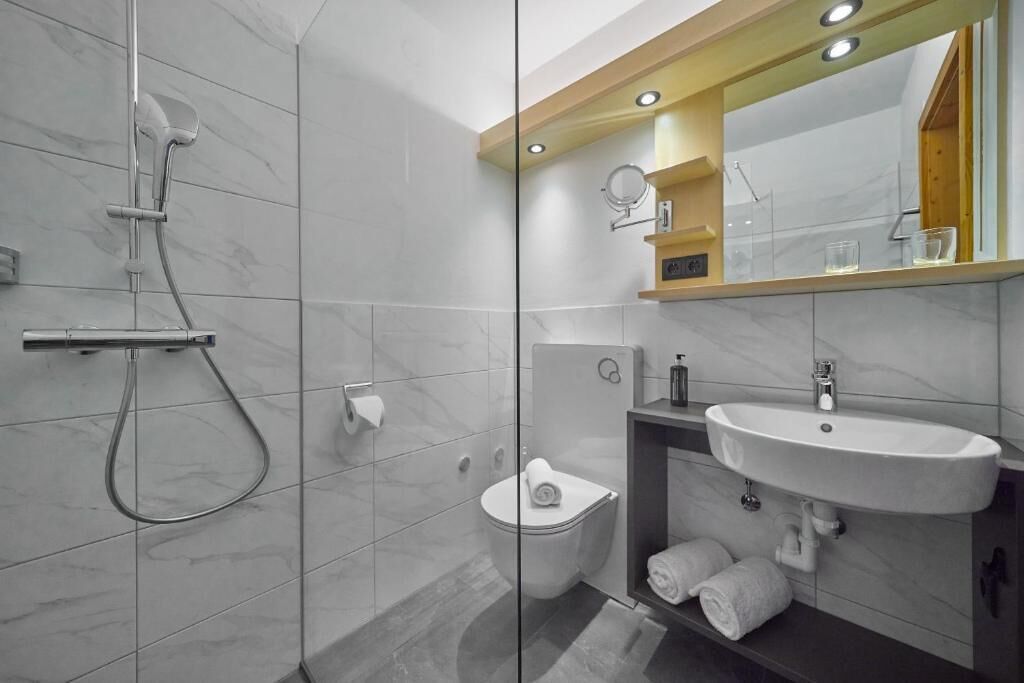 A modern bathroom with a glass-enclosed shower, a toilet, a sink, and a mirror above the sink.