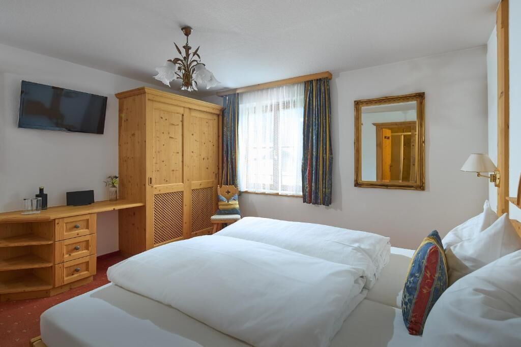 A hotel room with a bed, a desk, a wardrobe, a television, and a mirror.
