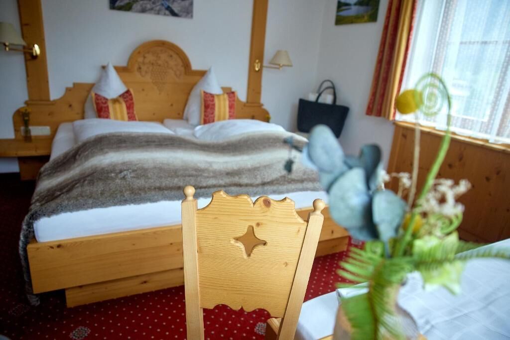 Un letto di legno con testiera, un comodino, una lampada, una tovaglia rossa con pois e una finestra con tende.