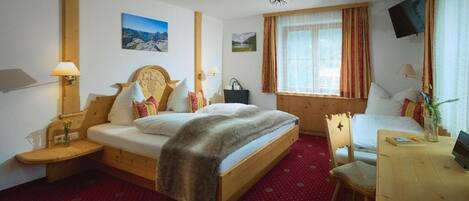 A hotel room with a bed, bedside tables, a desk, a chair, a TV, and a window with curtains.