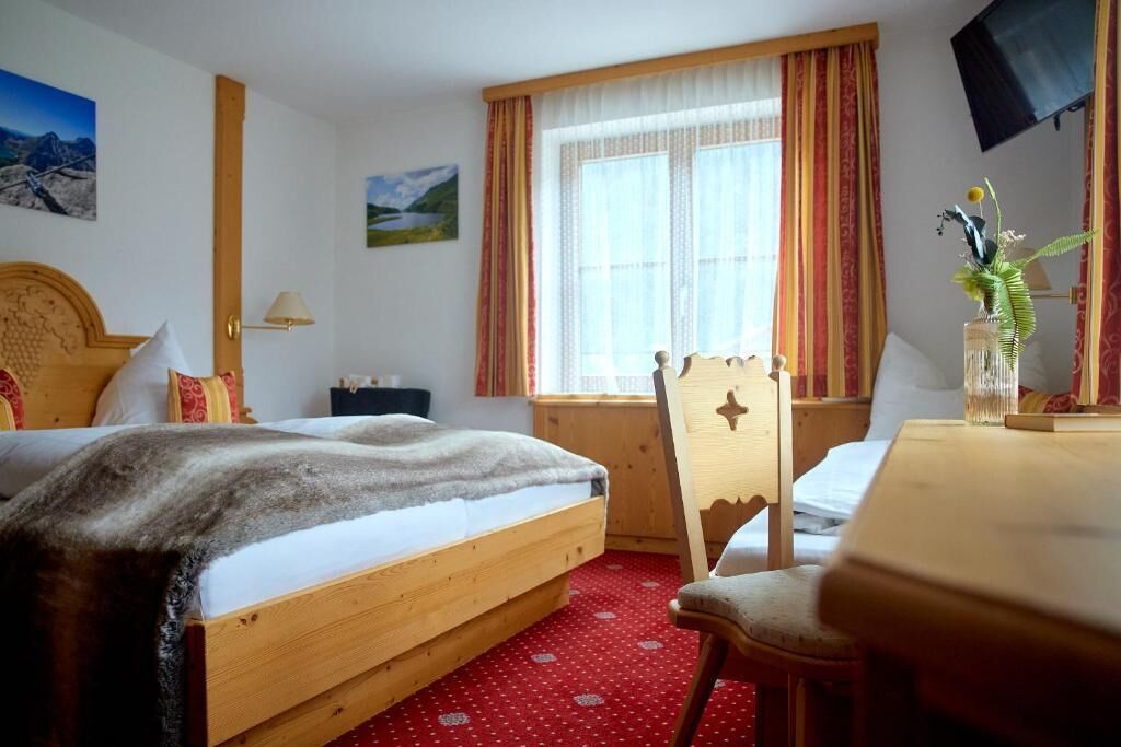 Une chambre d’hôtel comprenant un lit, un bureau, une chaise, une fenêtre avec des rideaux et un téléviseur fixé au mur.