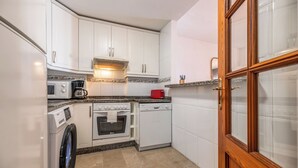 A compact kitchen with white cabinets, a microwave, a coffee maker, a red toaster, an oven, and a dishwasher. - LXR Marysol 2-Bedroom. Apt (Benalmádena)