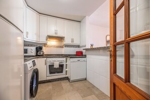 Eine kleine Küche mit weißen Schränken, einer Mikrowelle, einer Kaffeemaschine, einem roten Toaster, einem Backofen und einem Geschirrspüler.