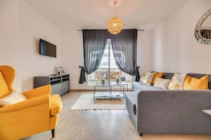 Ein modernes Wohnzimmer mit einer Couch, einem Sessel, einem Fernseher und einem Esstisch mit Stühlen.