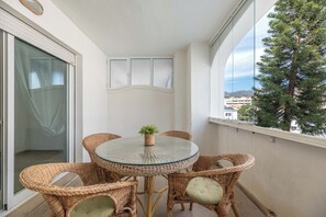 Een balkon met rieten meubilair, een glazen tafel en een plant in pot.
