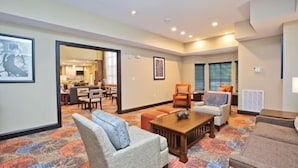 A spacious living area with a large sofa, a coffee table, and a dining table. There is a kitchen visible in the background.