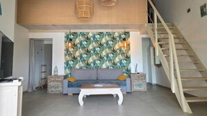 Una sala de estar con un sofá, una mesa de centro, dos mesitas auxiliares, una escalera y una pared con un diseño de hojas tropicales.