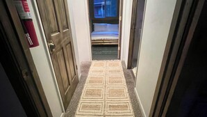 En smal hall med en mönstrad matta, trädörrar och en säng som syns i bakgrunden.