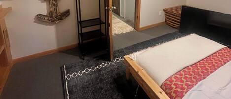 A bedroom with a sloped ceiling, a bed, a wooden bench, a hanging coat rack, and a ceiling fan.