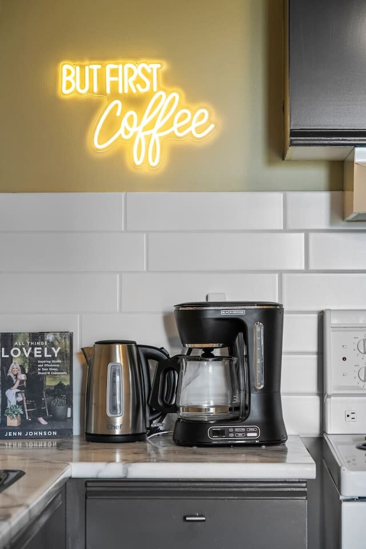 A kitchen with a coffee maker, a kettle, and a book titled 'All Things Lovely' by Jenn Johnson.