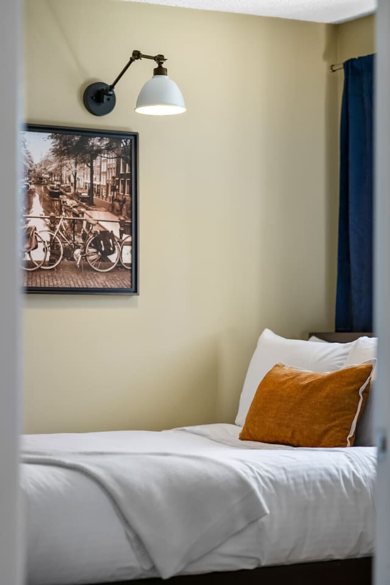 A bedroom with a bed, a wall-mounted lamp, and a framed picture.