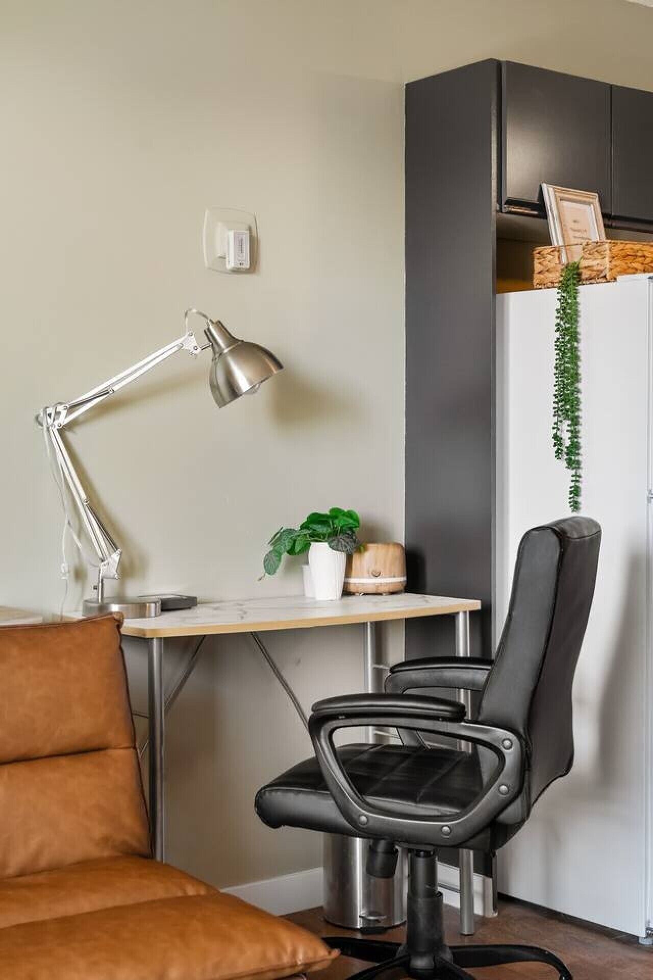 A modern office space with a desk, two chairs, a lamp, a plant, a coffee machine, and a refrigerator.