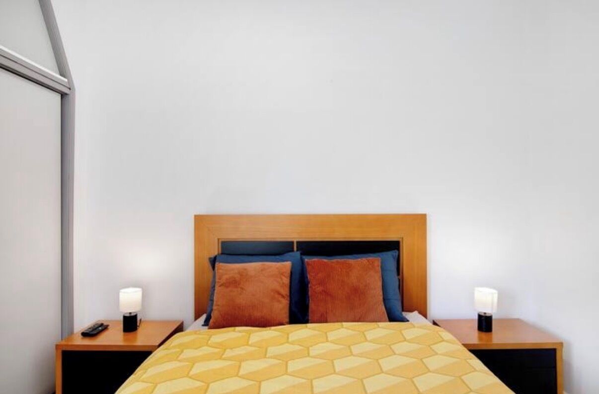 Ein Hotelzimmer mit einem hölzernen Kopfteil, einer gelb gemusterten Bettdecke und zwei Nachttischlampen.