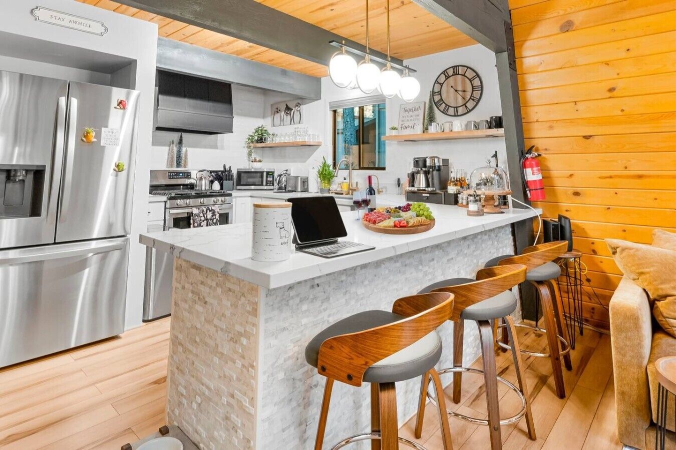 A modern kitchen with a central island, bar stools, a laptop, and a clock on the wall.