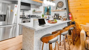 Eine moderne Küche mit einer zentralen Kochinsel, Barhocker, einem Laptop und einer Wanduhr.