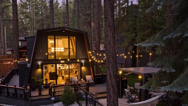 Eine moderne Hütte mit Glasfassade, Sitzgelegenheiten im Freien und einer Terrasse, die von Bäumen umgeben ist.